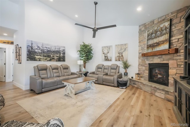 living room featuring ceiling fan, a fireplace, a high ceiling, and light wood-type flooring