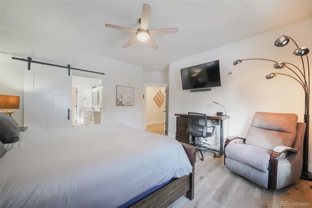 bedroom featuring light hardwood / wood-style floors, a barn door, ceiling fan, and ensuite bathroom