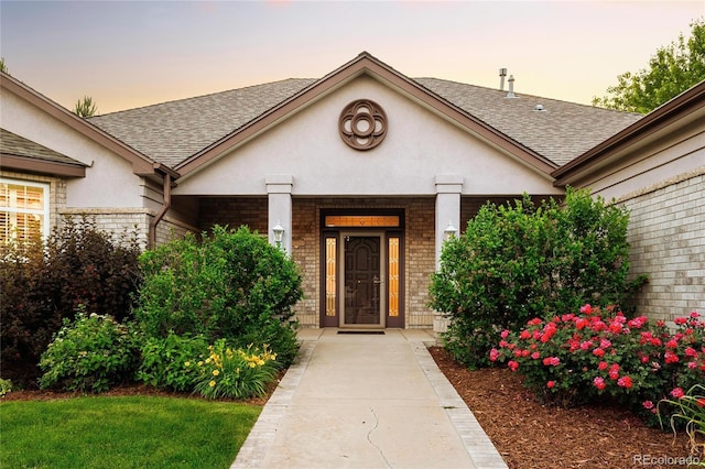 3231 Oak St, Wheat Ridge, CO 80033 - view of exterior entry featuring stucco siding, roof with shingles, and brick siding