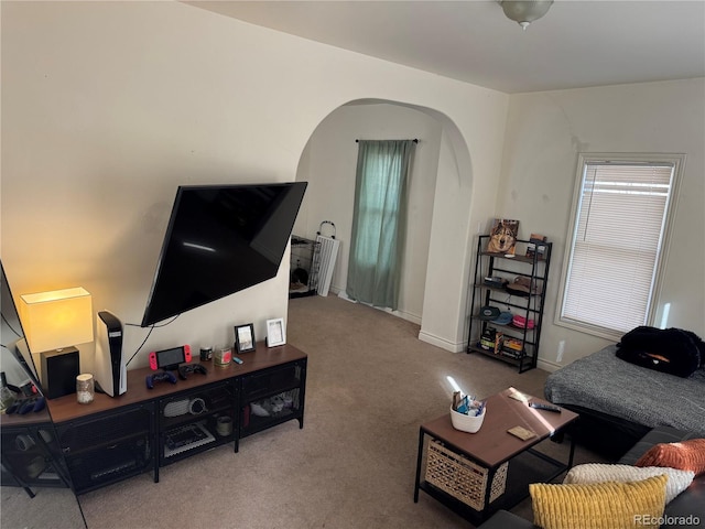 living area featuring carpet flooring, baseboards, and arched walkways