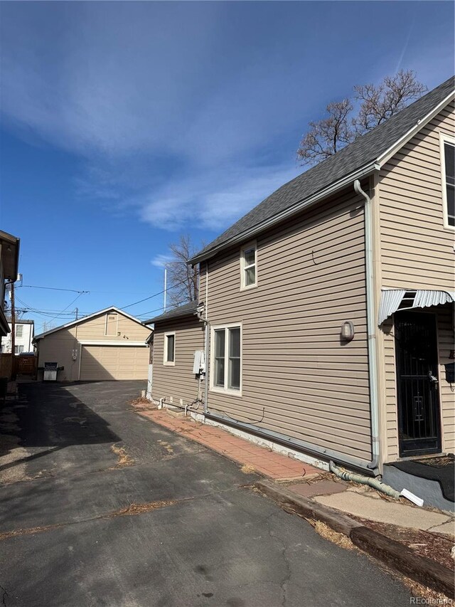 view of side of property with an outbuilding, a garage, and roof with shingles