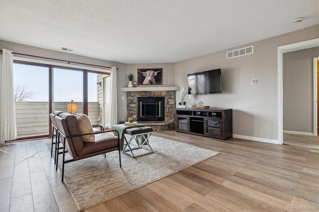living area featuring baseboards, a fireplace, light wood-style flooring, and visible vents