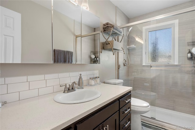 bathroom with vanity, toilet, a shower with door, and backsplash