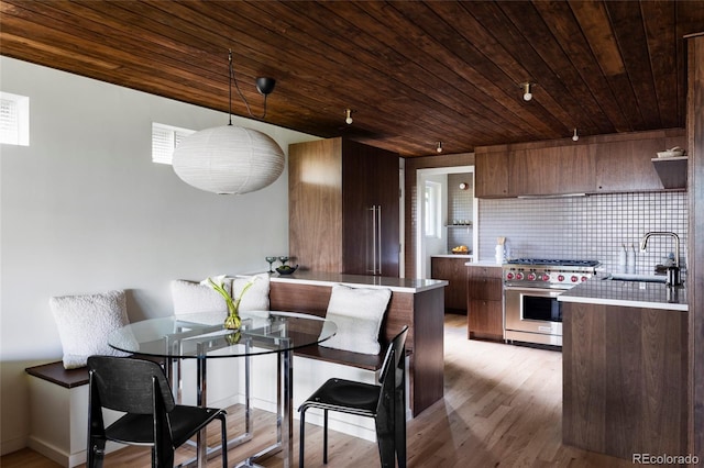 kitchen featuring a sink, backsplash, luxury stove, light wood finished floors, and light countertops