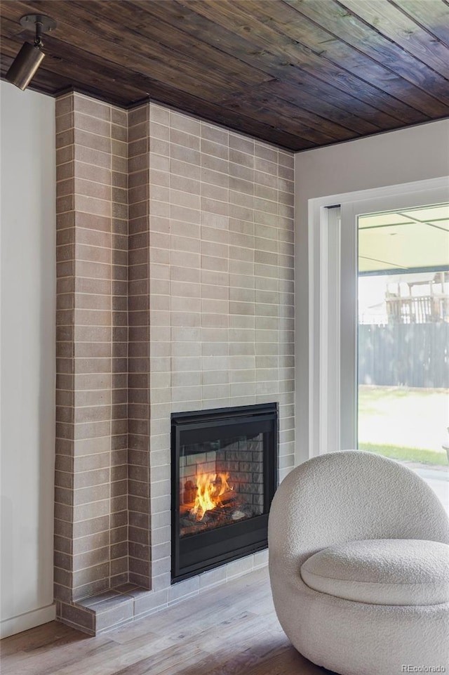 living area with wood ceiling, wood finished floors, and a lit fireplace