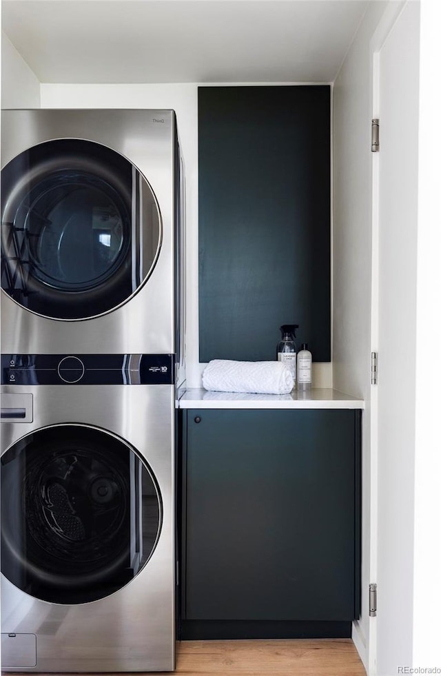 clothes washing area with laundry area, light wood-style flooring, and stacked washing maching and dryer