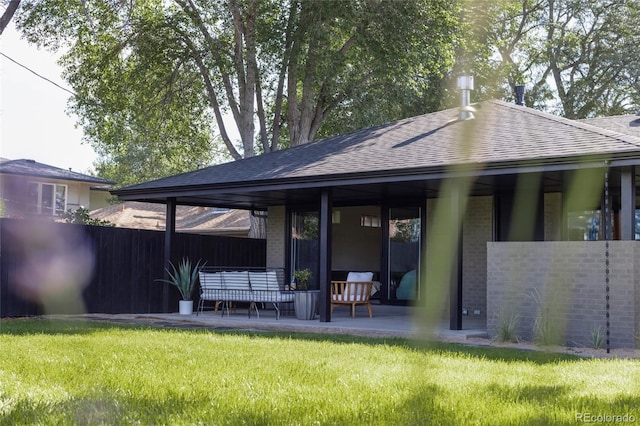 back of property with a patio area, brick siding, a lawn, and roof with shingles