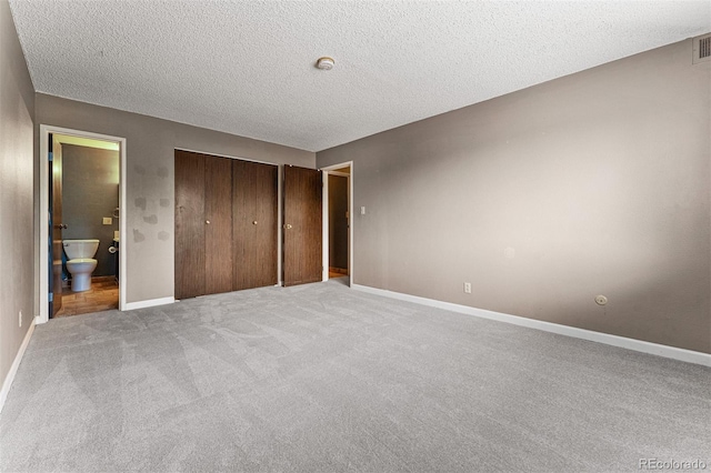 unfurnished bedroom featuring ensuite bathroom, light colored carpet, a textured ceiling, and a closet