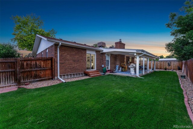 12906 Cherry Way, Thornton, CO 80241 - back of property at dusk with a chimney, brick siding, a patio area, and a fenced backyard