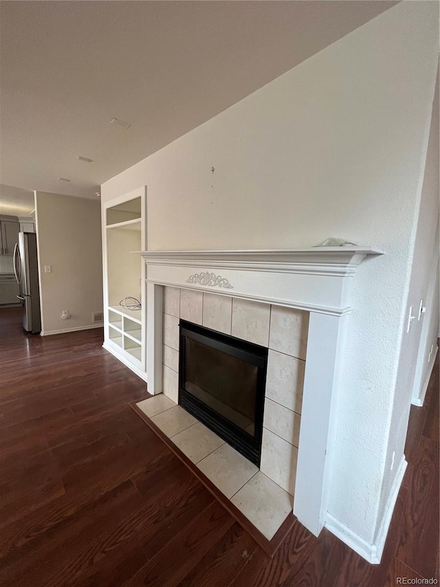 details featuring visible vents, a tiled fireplace, wood finished floors, freestanding refrigerator, and baseboards