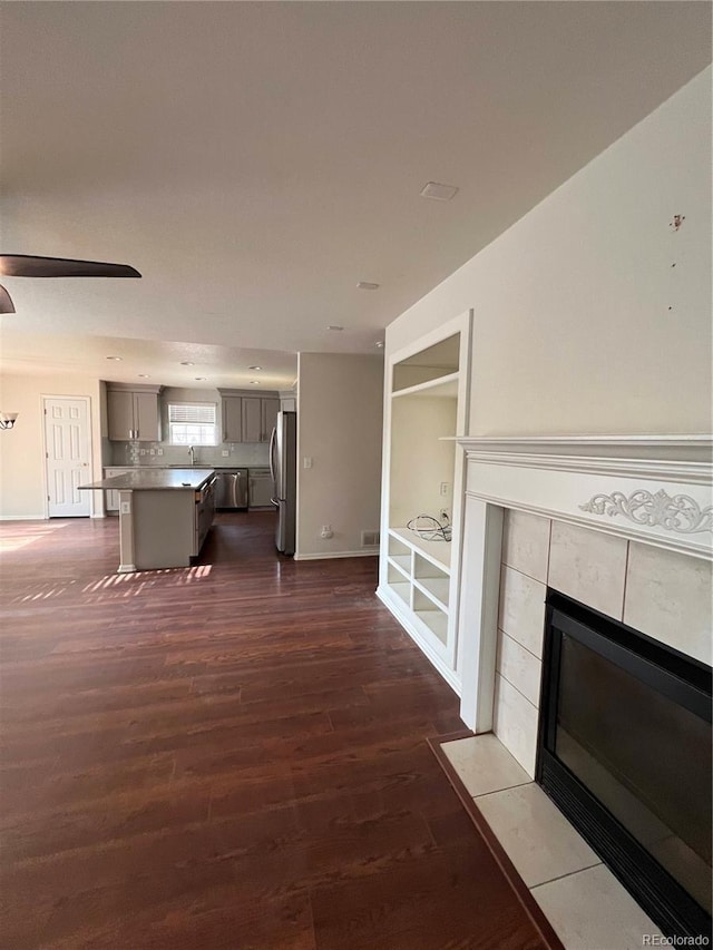 unfurnished living room with visible vents, baseboards, a fireplace, dark wood-style flooring, and a sink