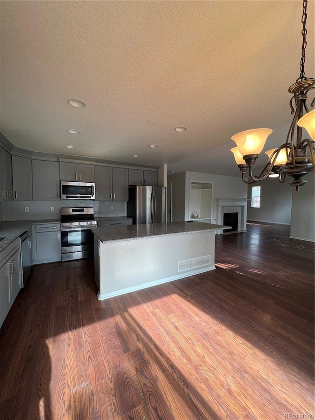 kitchen featuring visible vents, gray cabinetry, a kitchen island, stainless steel appliances, and dark wood-style flooring