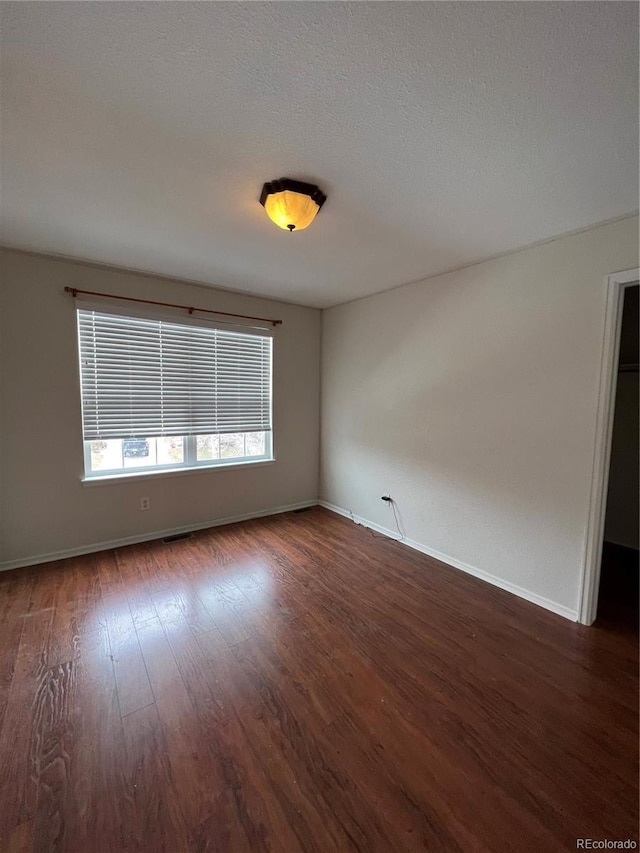 unfurnished room featuring a textured ceiling, baseboards, and wood finished floors