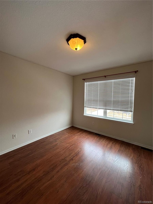 spare room featuring dark wood-type flooring, baseboards, and a textured ceiling