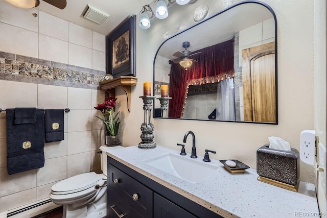 bathroom featuring ceiling fan, toilet, vanity, tile walls, and baseboard heating