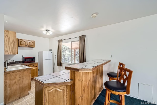 kitchen with tile countertops, a breakfast bar area, freestanding refrigerator, a peninsula, and a sink