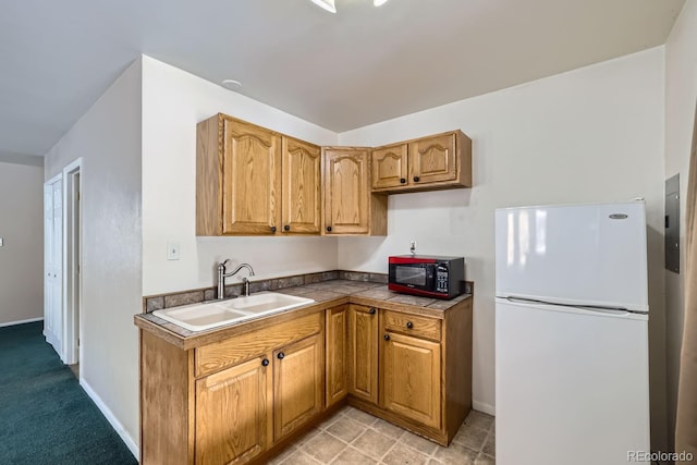 kitchen with brown cabinetry, a sink, freestanding refrigerator, and baseboards