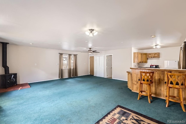 carpeted living area with a ceiling fan, a wood stove, and a bar