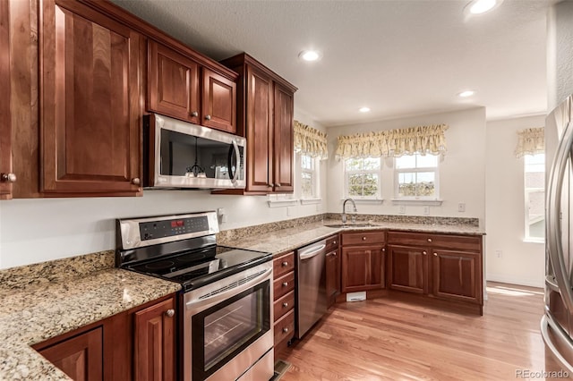 kitchen featuring appliances with stainless steel finishes, a sink, light wood-type flooring, light stone counters, and recessed lighting