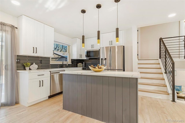 kitchen featuring hanging light fixtures, appliances with stainless steel finishes, white cabinetry, a kitchen island, and light hardwood / wood-style floors