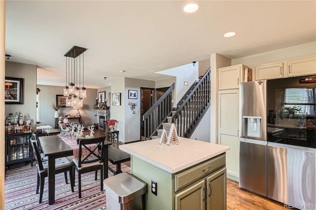 kitchen featuring pendant lighting, stainless steel refrigerator with ice dispenser, green cabinetry, light hardwood / wood-style floors, and a kitchen island