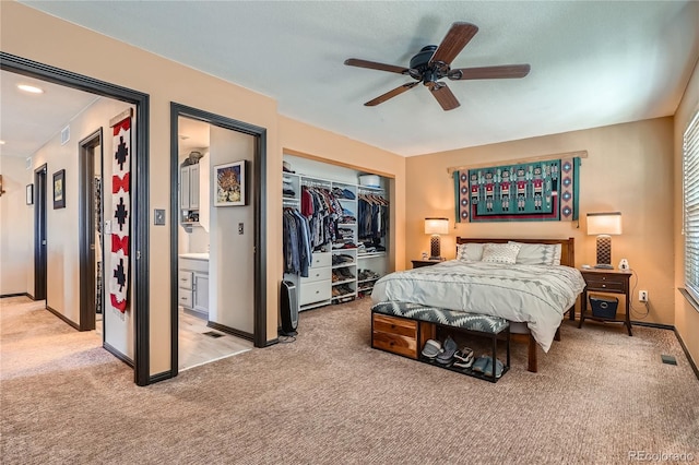 carpeted bedroom featuring a closet, ensuite bath, and ceiling fan