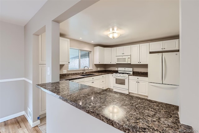 kitchen featuring white cabinetry, sink, kitchen peninsula, dark stone countertops, and white appliances