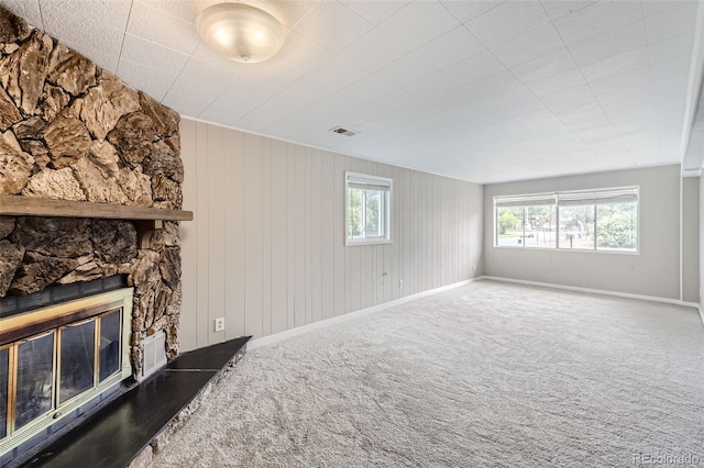 unfurnished living room with a fireplace, carpet flooring, and wooden walls