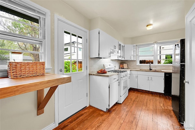 kitchen with white gas range, a sink, under cabinet range hood, light wood finished floors, and black dishwasher