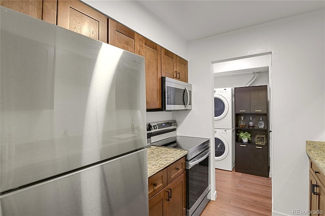 7995 E Mississippi Ave Unit K3, Denver, CO 80247 - kitchen featuring appliances with stainless steel finishes, estacked washer and dryer, light wood-style floors, brown cabinets, and light stone counters