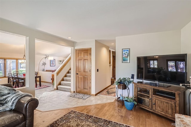 living room featuring baseboards, stairway, a chandelier, and light wood-style floors