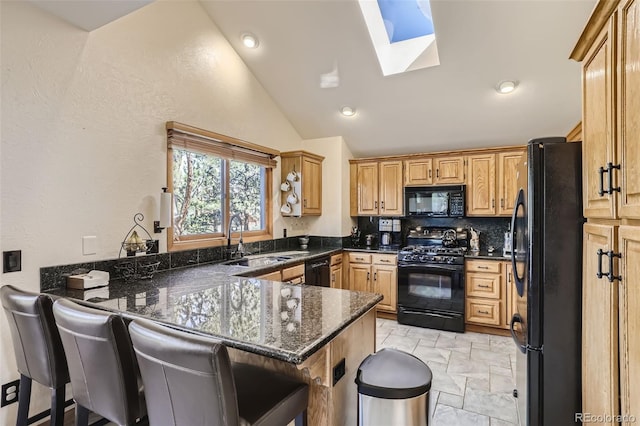 kitchen with a breakfast bar area, a sink, dark stone countertops, a peninsula, and black appliances