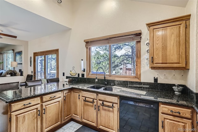 kitchen with black dishwasher, open floor plan, dark stone countertops, a peninsula, and a sink