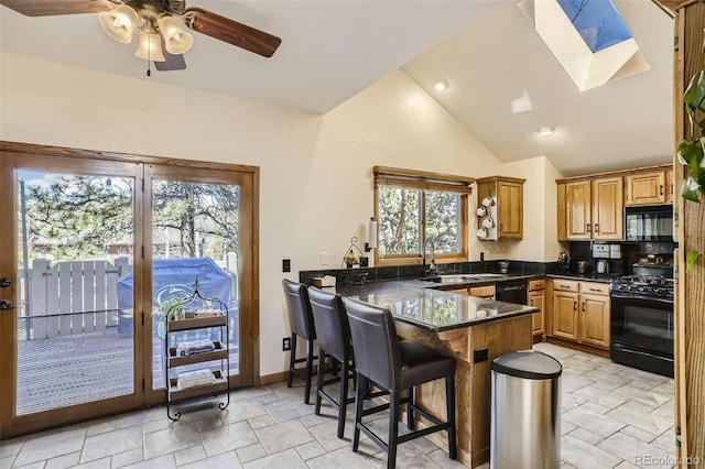 kitchen with dark stone counters, a peninsula, black appliances, a kitchen bar, and a sink