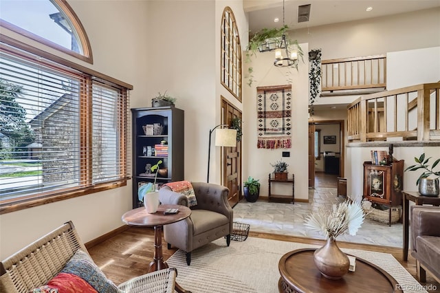 living area with light wood-type flooring, baseboards, a notable chandelier, and a high ceiling