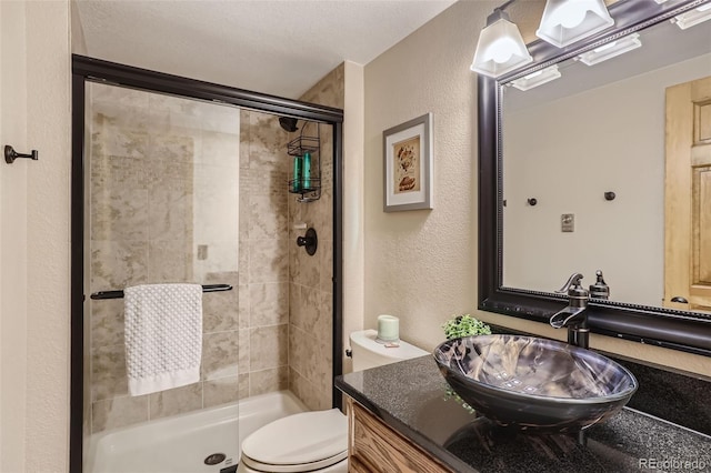 bathroom featuring a stall shower, a textured wall, vanity, and toilet