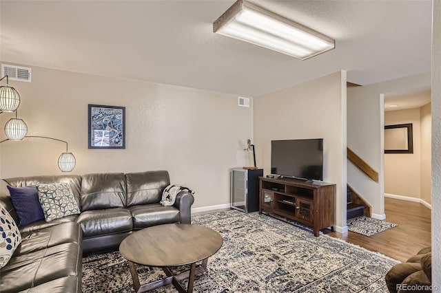 living room featuring stairs, wood finished floors, visible vents, and baseboards