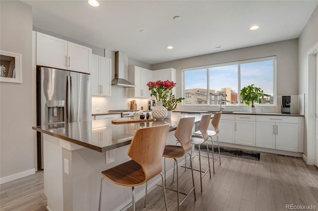 kitchen with white cabinets, stainless steel fridge, light wood finished floors, and wall chimney exhaust hood