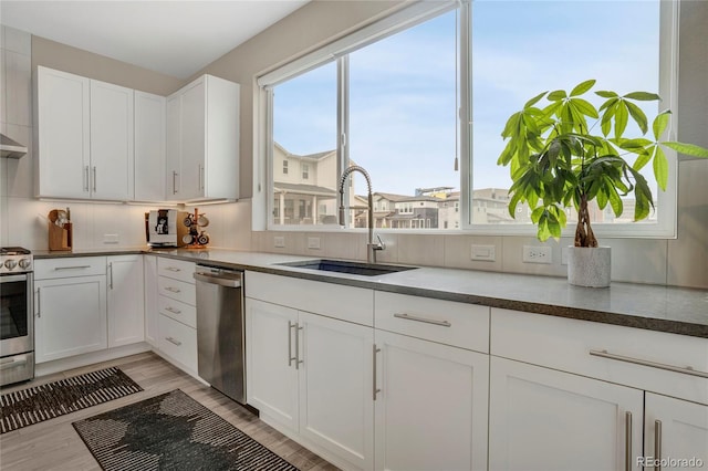 kitchen with a sink, light wood finished floors, white cabinets, and stainless steel appliances