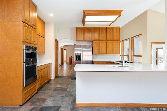 6668 Fairways Dr, Longmont, CO 80503 - kitchen featuring arched walkways, appliances with stainless steel finishes, a peninsula, light countertops, and brown cabinetry