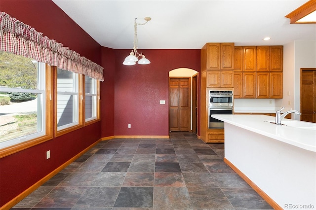 6668 Fairways Dr, Longmont, CO 80503 - kitchen featuring double oven, a sink, arched walkways, brown cabinets, and baseboards