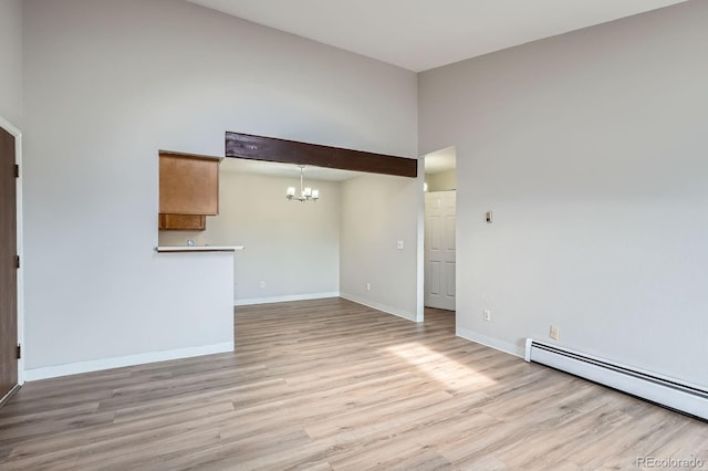 unfurnished room with a chandelier, a baseboard radiator, light wood finished floors, baseboards, and a towering ceiling