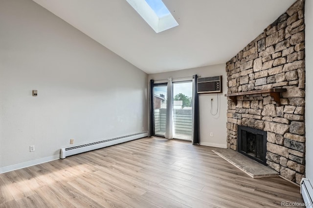 unfurnished living room with baseboard heating, a wall mounted AC, vaulted ceiling, a skylight, and a stone fireplace