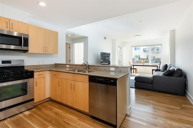 kitchen featuring light stone counters, stainless steel appliances, kitchen peninsula, and light brown cabinets