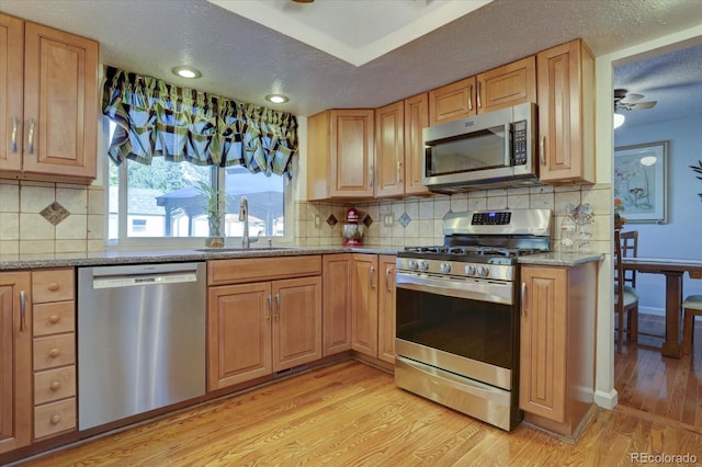 kitchen with sink, light hardwood / wood-style flooring, ceiling fan, light stone counters, and stainless steel appliances