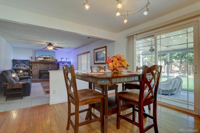 dining space with a fireplace, light hardwood / wood-style flooring, and ceiling fan