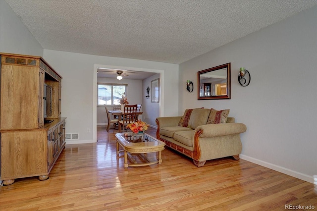 living room with ceiling fan, light wood-type flooring, and a textured ceiling