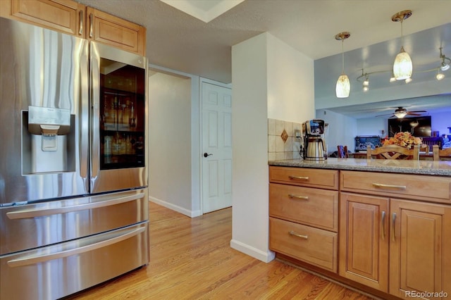 kitchen with stainless steel refrigerator with ice dispenser, light stone counters, ceiling fan, decorative light fixtures, and light hardwood / wood-style flooring