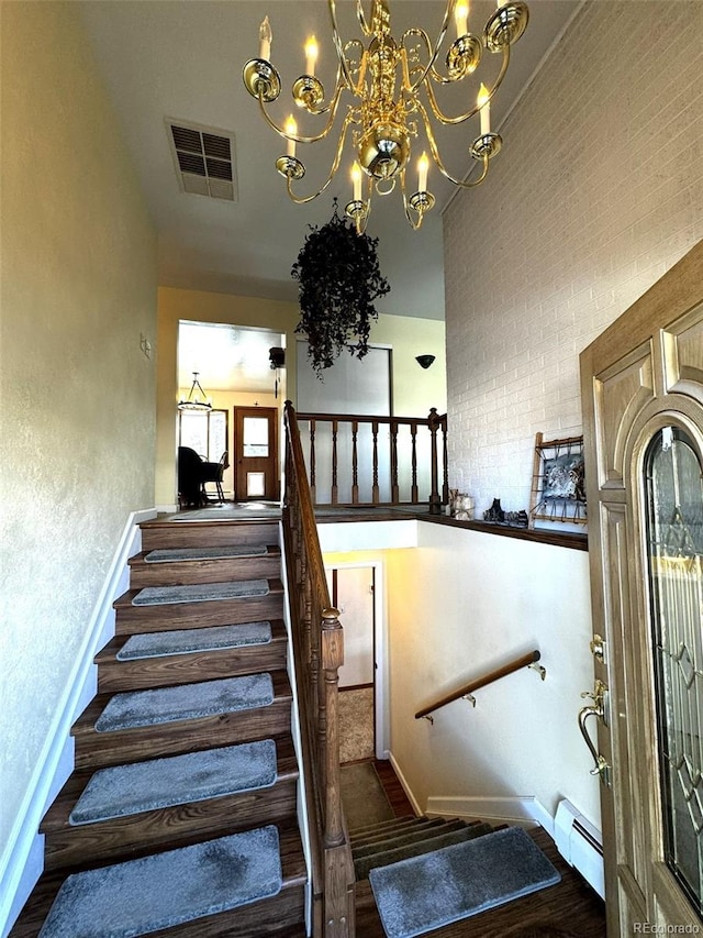 staircase with a high ceiling, baseboard heating, an inviting chandelier, and wood-type flooring