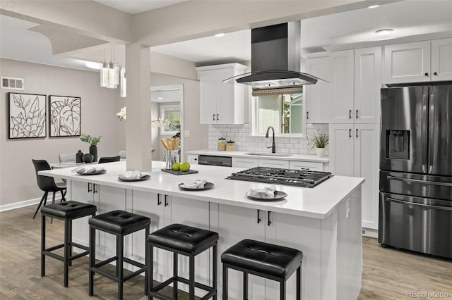 1120 S Harrison St, Denver, CO 80210 - kitchen with appliances with stainless steel finishes, island range hood, a kitchen breakfast bar, and light wood-type flooring